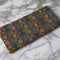 Set of four dark green cloth napkins with a repeating pattern of golden beetles, coral flowers, and ochre wildflowers in an intricate botanical and entomological design.